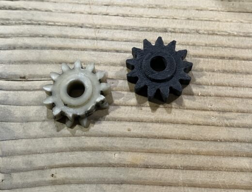 Deux engrenages en plastique, l'un blanc et l'autre noir, posés sur une surface en bois rainuré.